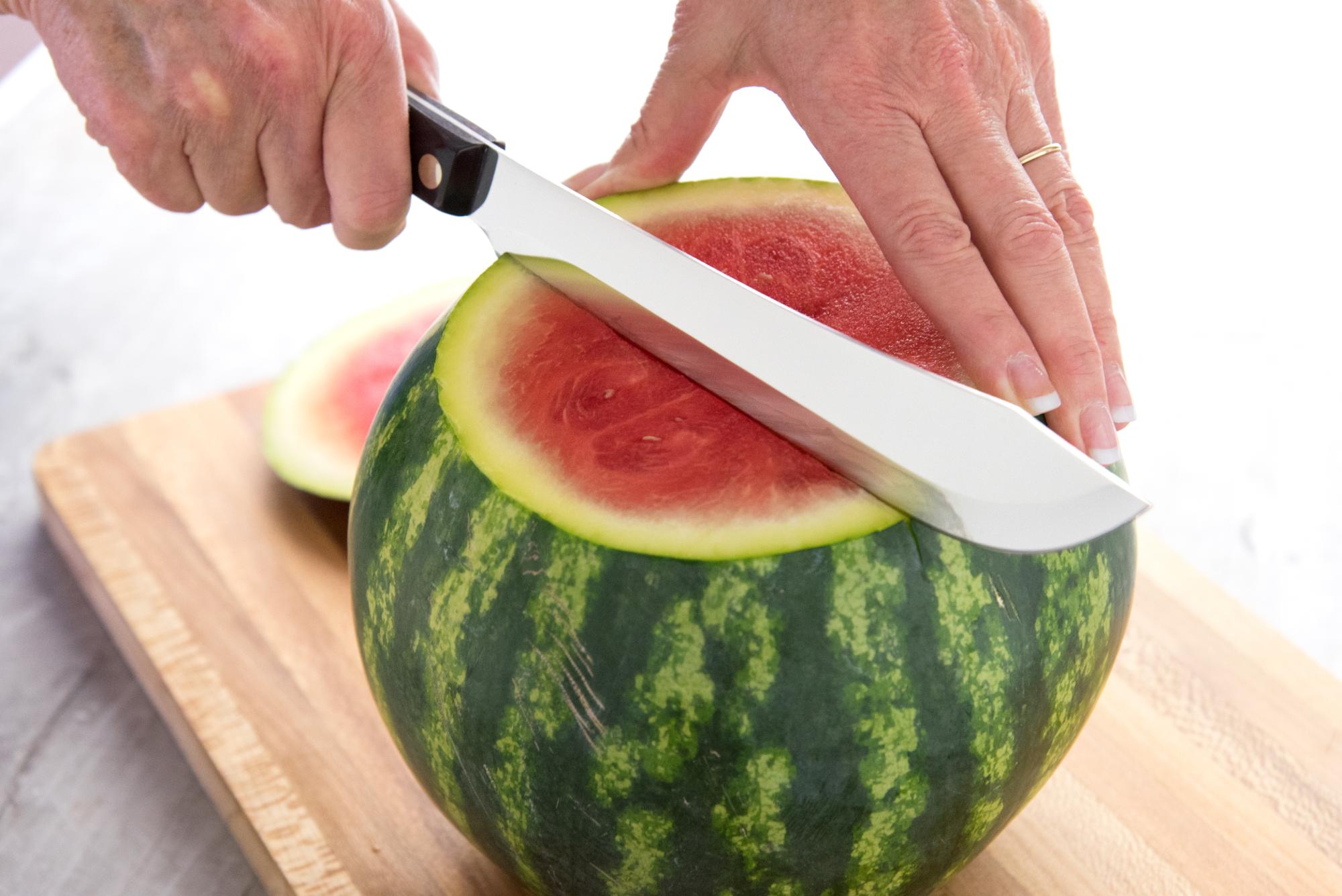 Using a Butcher knife to cut the watermelon in half.