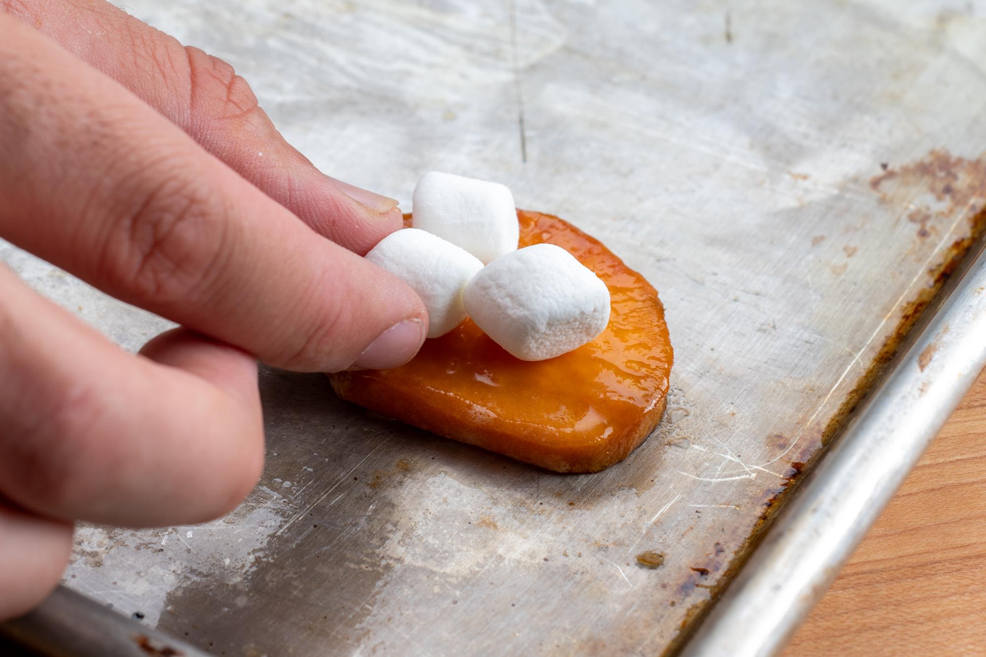 Putting marshmallows on the sweet potato slices.