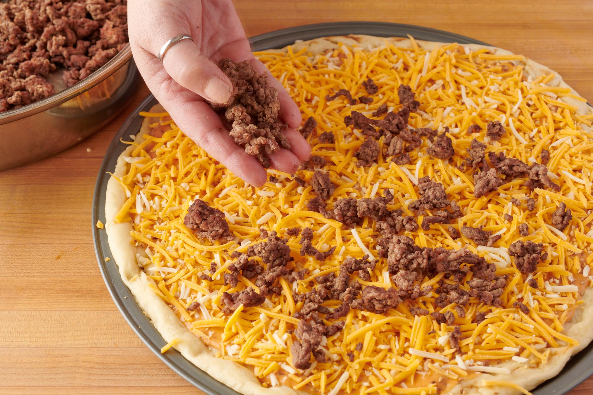 Sprinkling the ground beef on the pizza.