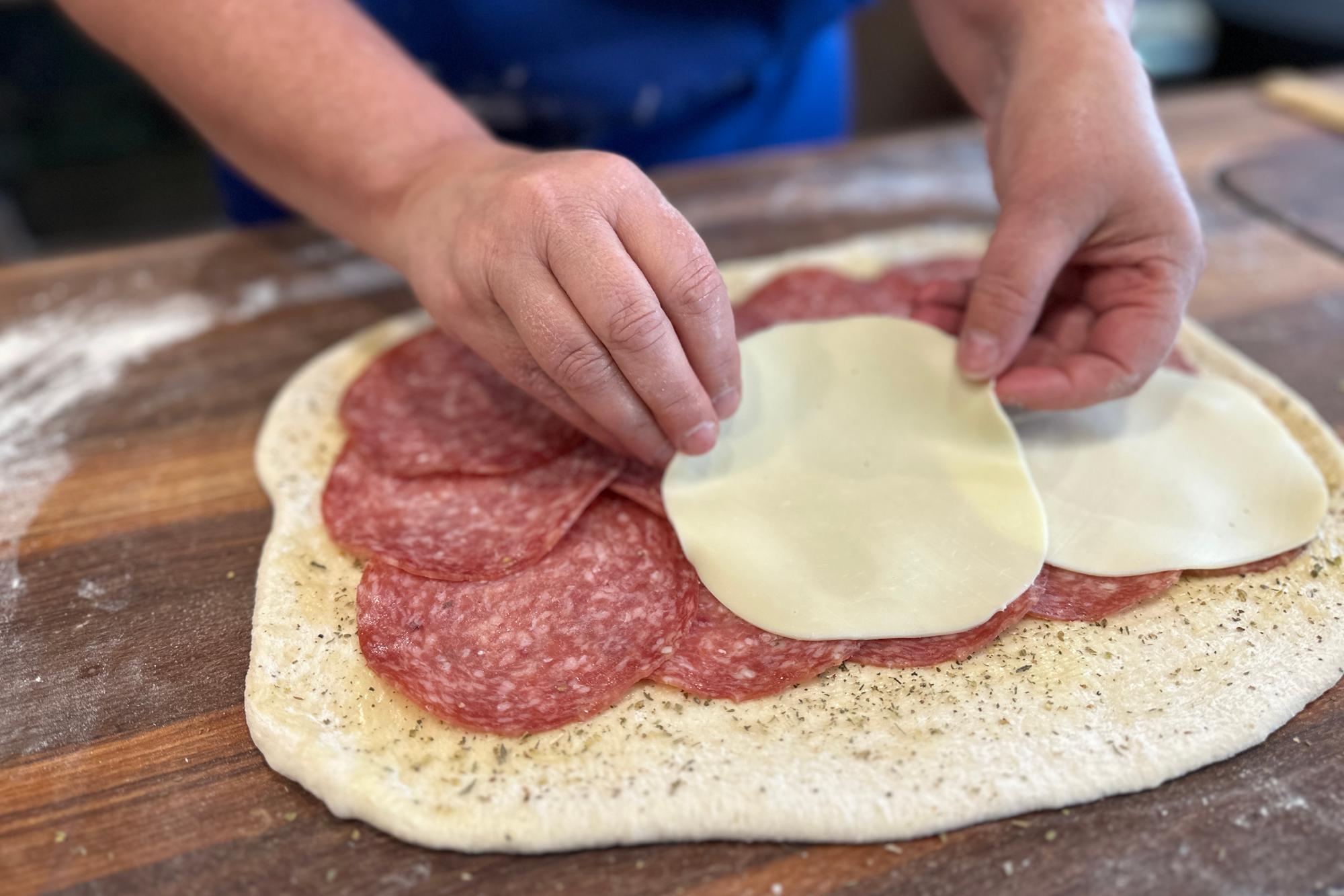 Layering provolone on top of the salami.