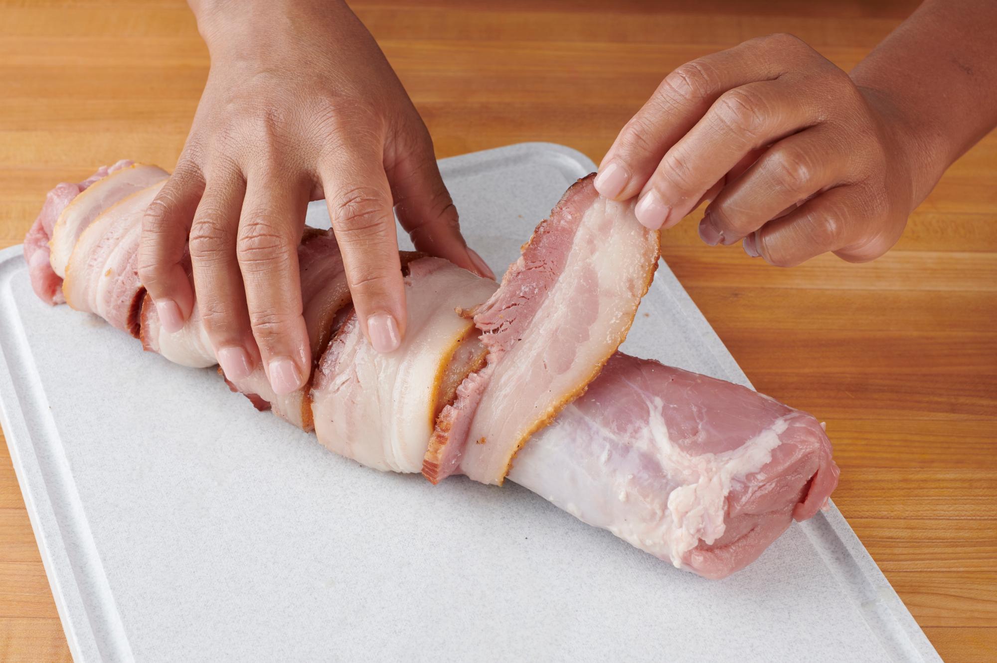 Wrapping the tenderloin with bacon.