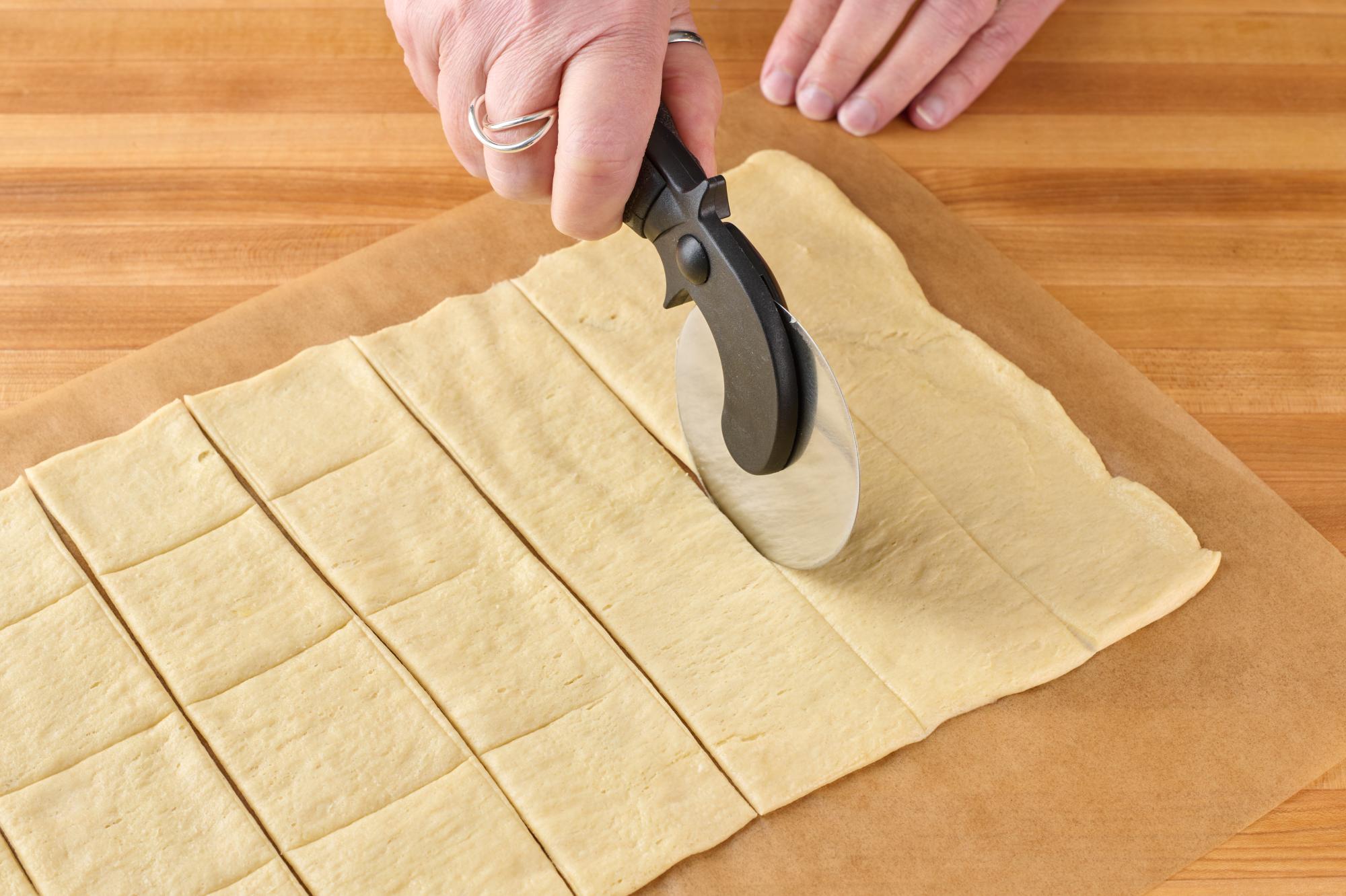Using a Pizza Cutter to cut the dough into squares.