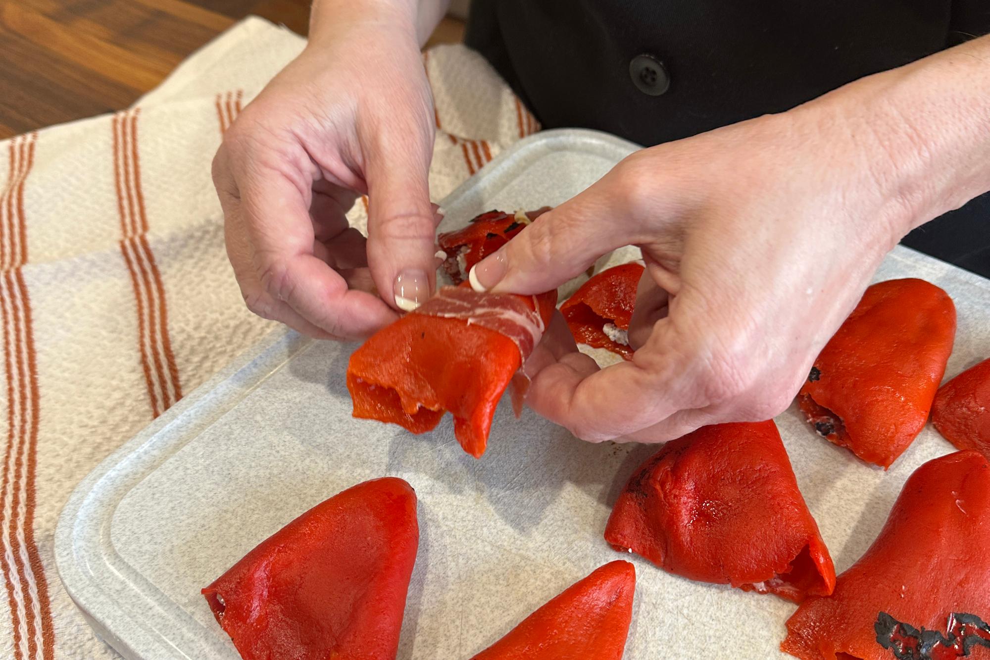 Wrapping prosciutto around stuffed pepper.