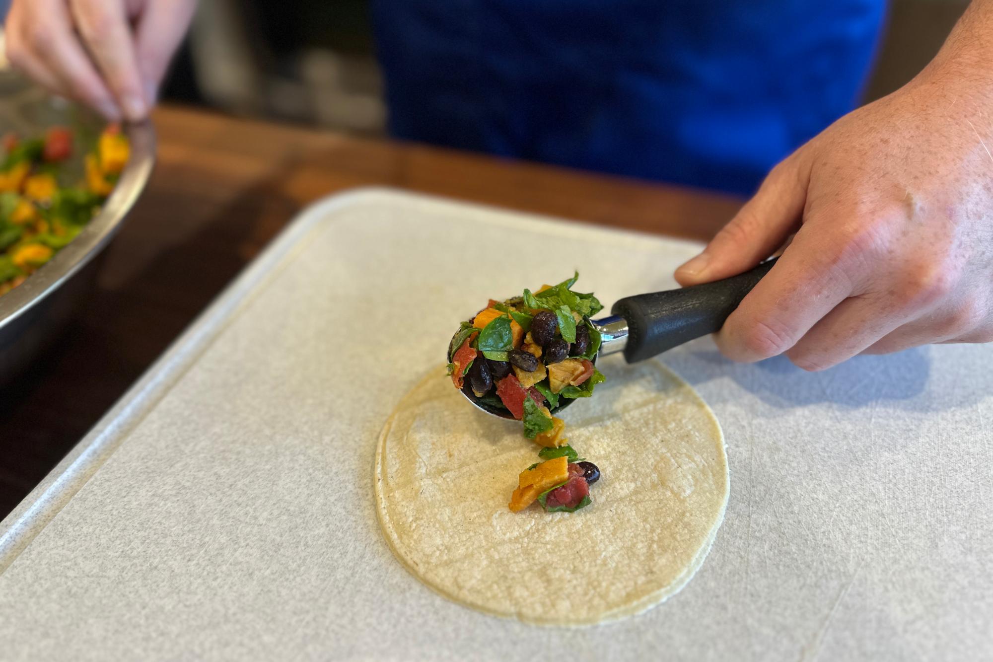 Placing Ice Cream Scoop full of sweet potato mixture onto tortilla.